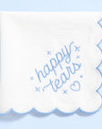 White scalloped edge napkin with 'happy tears' text on a light blue background