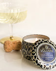 Crisp champagne tin candle burning next to champagne cork and coupe.