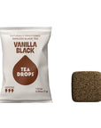 A white bag of Tea Drops Vanilla Black naturally sweetened bagless black tea next to a single square-shaped brown tea drop on a plain white background.