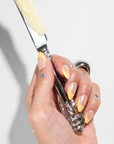 Hand holding a silver and cream-colored tool against a light gray background