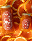Two jars of marmalade with a visible brand label on a background of sliced oranges.