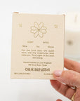 Hand holding a small beige box with text and a flower design, featuring the brand 'Ollie Blossom'.