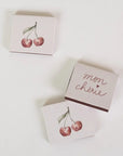 Three small rectangular boxes arranged on a white background. Two boxes feature a watercolor-style red cherry illustration, and one box has the words 'mon chârie' in metallic rose-gold script.