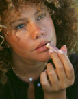 Woman applying lipstick outdoors with a blurred natural background