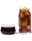 Glass of iced coffee with a splash next to a cup of black coffee on a white background