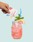 pouring packet into mason jar filled with pink lemonade and garnished with a pink lemon