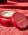 red tin candle with gold sparkles on it on a shiny red tablecloth