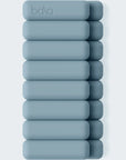 A stack of ten matte blue-gray rectangular bath blocks with rounded corners, arranged vertically on a light gray background. The top block features the debossed brand name 'baha'.