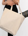 Person holding a beige tote bag with a yoga mat over their shoulder on a white background