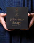 person in a blue shirt holding a black box of the musee palo santo and sage shower steamers