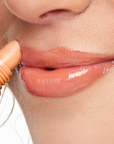 Close-up of a person applying lip gloss to their lips.