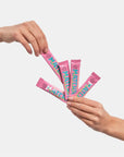 Two hands holding pink packets with colorful text against a light gray background