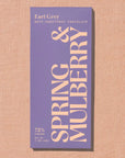 A single chocolate bar package labeled 'Earl Grey' and 'SPRING & MULBERRY' stands upright on a textured beige surface. The wrapper is lavender-purple with large cream lettering and small text reading 'DATE-SWEETENED CHOCOLATE'.