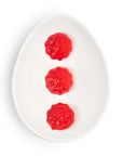 Three red gummy bears on a white plate with a white background
