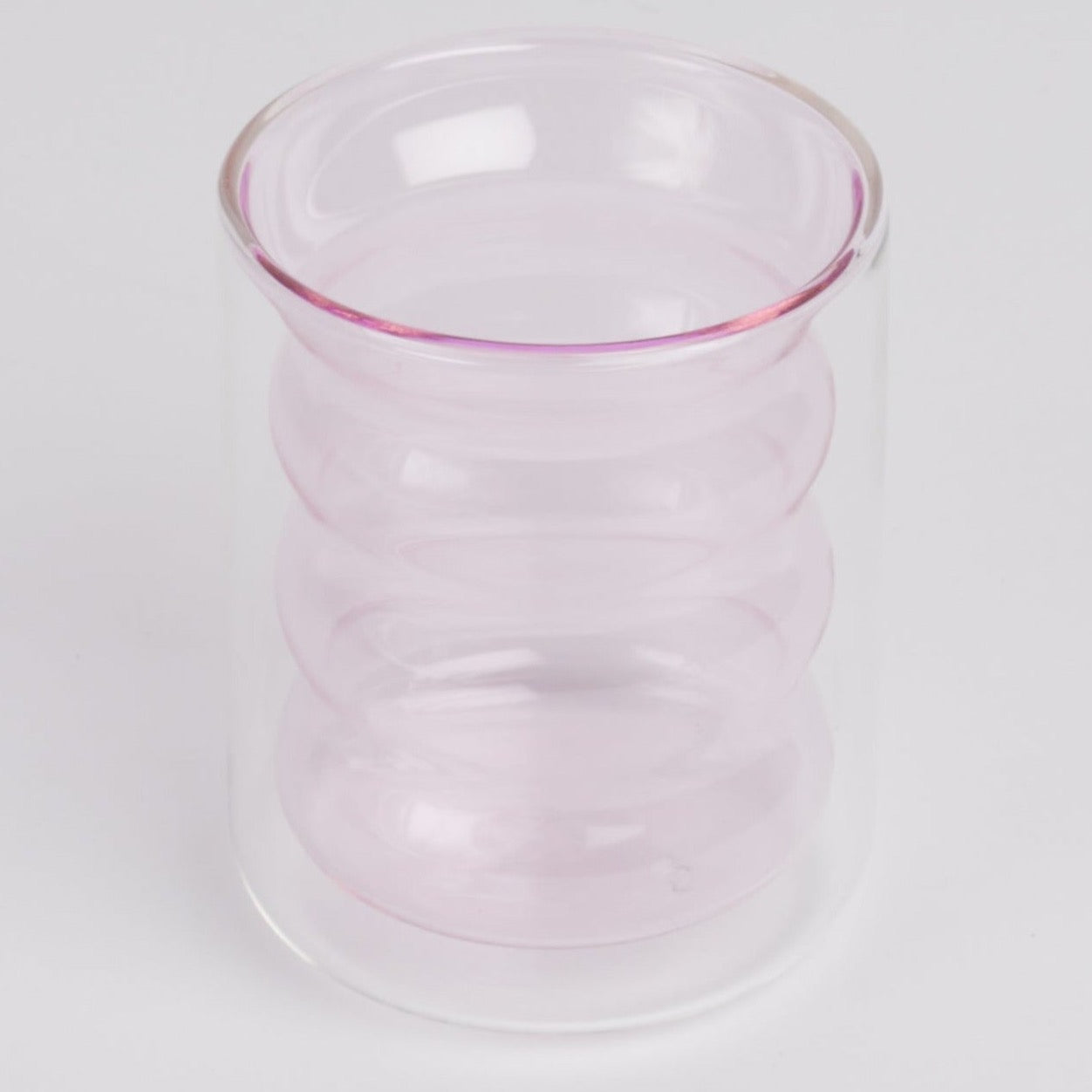 A double-walled light pink rippled glass standing upright shot against a white background.