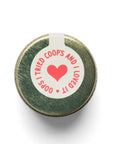 Round green metal object with a white label featuring a red heart and text on a white background