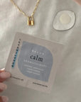 Aromatherapy inhalation tab labeled 'Relax Calm' held by a hand with a gold necklace in the background.