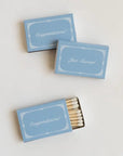 Three light blue matchboxes with white decorative borders and script text reading Congratulations, Just Married, and Congratulations, arranged on a plain light background. One matchbox is open and shows white matches inside.