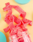 Pink gummy worms spilling out of a container on a yellow background