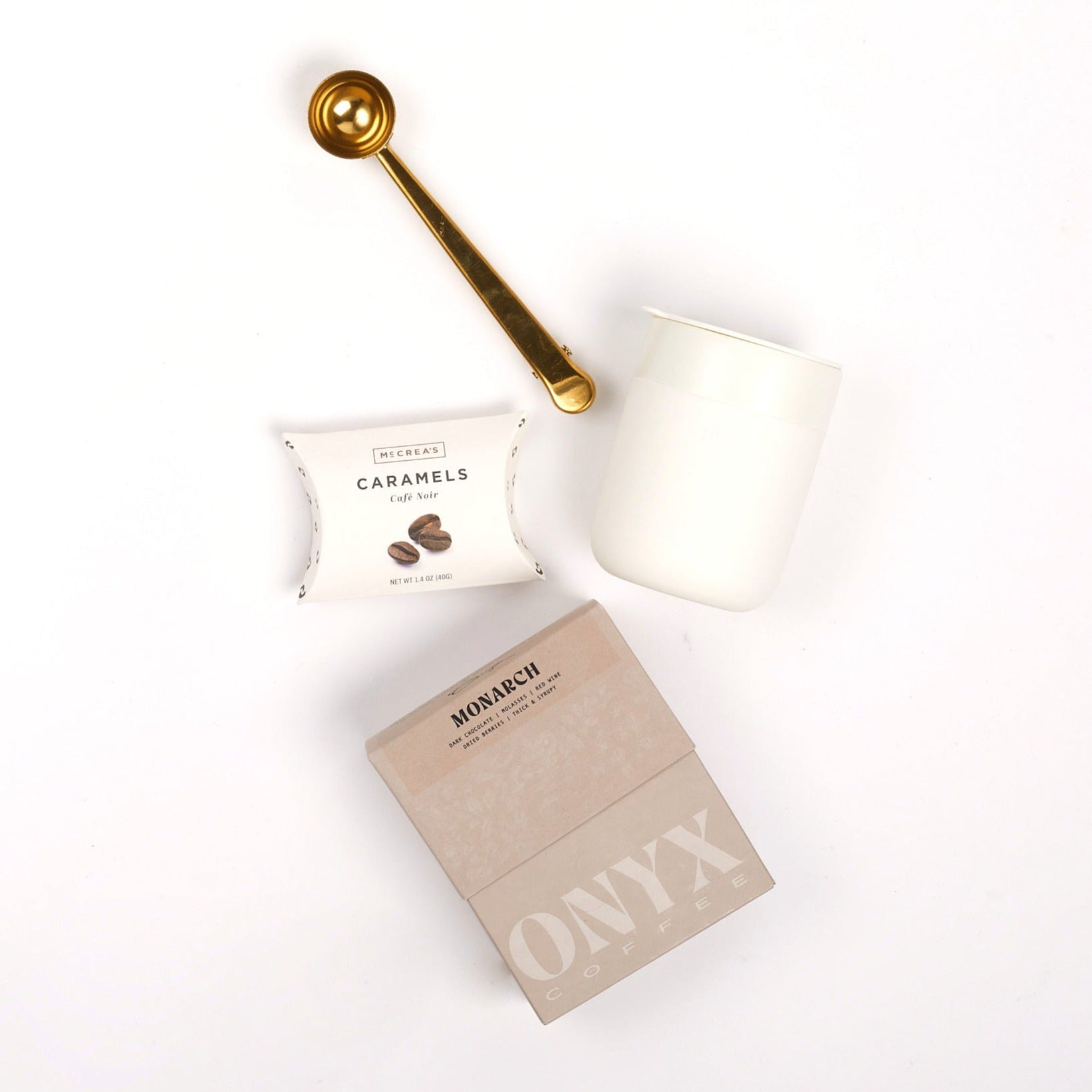 Gold coffee scoop, coffee caramels, cream mug and box of coffee on white background