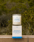 Candle and packaging labeled 'Mornings at the Lake House' on a wooden surface with a natural background.