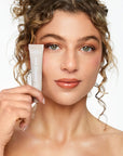 Woman holding a skincare product against a neutral background