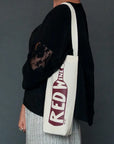 Person holding a white tote bag with 'Red Wine' text against a gray background