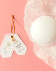 White bath bomb with a tag on a pink background