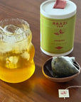 raazi jasmine green tea on a wood table next to a glass and sachet