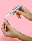 Person using a blue marker to write on a small object against a pink background