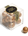 A clear acrylic cube box filled with gold-glittered espresso martini truffles, with a black and gold houndstooth ribbon label. A single truffle sits outside the box on a clean white background.