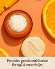 Small jar of lip scrub with a gold lid on an orange background with sliced oranges.