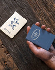 Hand holding a blue card with branding on a wooden surface
