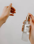 Person holding a perfume bottle with a gold cap against a plain background