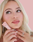 Woman holding a pink makeup product with a visible brand logo against a pink background