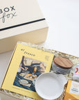 Gift box with 'Box Fox' branding, containing a book, bowl, and other items on a light background.