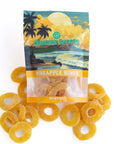A bag of Hawaiian Sweets Pineapple Rings candy with several loose yellow-orange ring-shaped gummy candies scattered in front on a white background.