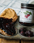 Jar of raspberry jam with a muffin and peanut butter on a wooden surface