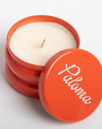 Candle in an orange container with 'Paloma' branding on a light gray background