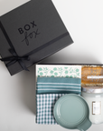 Gift box with 'Box Fox' branding containing folded fabric and a candle on a light gray background