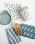 Collection of kitchen items including a candle, soap bottle, and cloths on a white background
