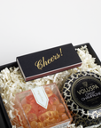 Gift set with Voluspa candle, gummy bears, and 'Cheers!' card in a box.