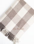 Plaid blanket with fringes and 'The Sweaters' branding on a white background
