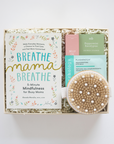 Product set with 'Breathe Mama Breathe' book, oil, and bath brush in a box on a white background