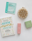 Collection of self-care products including a book, patch, oil, and pebbles on a white surface