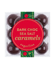 A clear square plastic box of Sugarfina Dark Choc Sea Salt Caramels, featuring eight glossy dark chocolate candies and a prominent red circular label with gold lettering and a green decorative ribbon.
