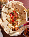 Platter of hummus with pita bread and various spreads on a wooden table