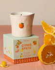 Candle with a citrus spritz theme on a pink surface