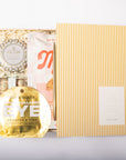 A curated beauty gift set arranged on a white background, featuring a gold Notem envelope, a gold round eye mask, a white and pink pouch, and a boxed set with shredded paper filler and a round Voluspa item.