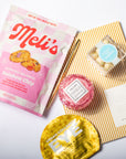 Meli's cookie package with a pink and gold product, and a striped napkin with a small dish on a white background.